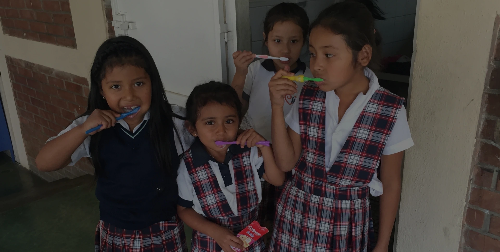 preventive dental care children Two young girls in school uniforms brushing their teeth with toothbrushes in front of a