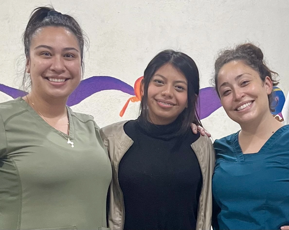dental charity Guatemala Three women in front of a white wall with a purple and orange design, smiling and posing for a photo